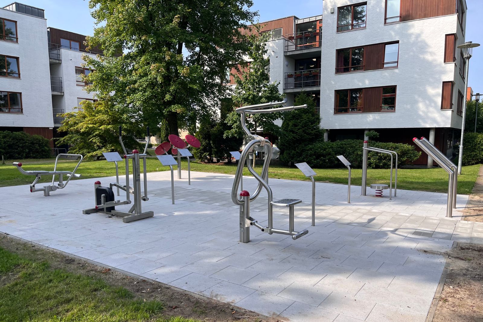 Barrierefreier Outdoor-Fitnesspark mit verschiedenen Trainingsgeräten zwischen Wohnhäusern.