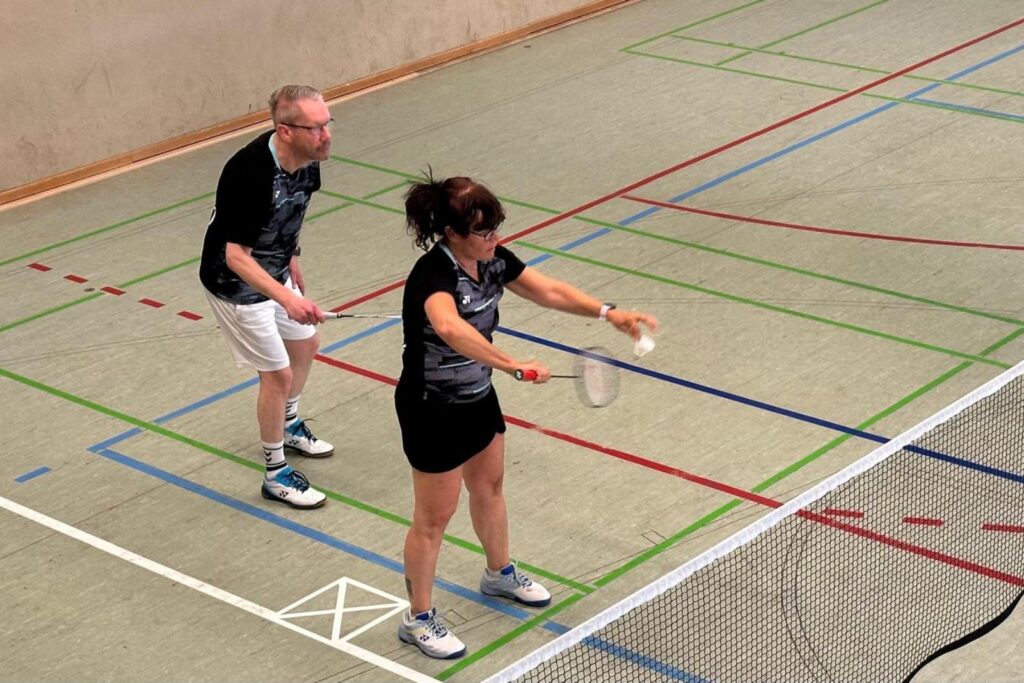 Zwei Spielende bereiten sich konzentriert auf einen Badmintonaufschlag am Netz vor.