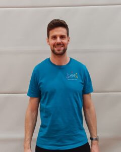 Ein Mann mit Bart lächelt in die Kamera und trägt ein türkisfarbenes ISV Alsterdorf T-Shirt.