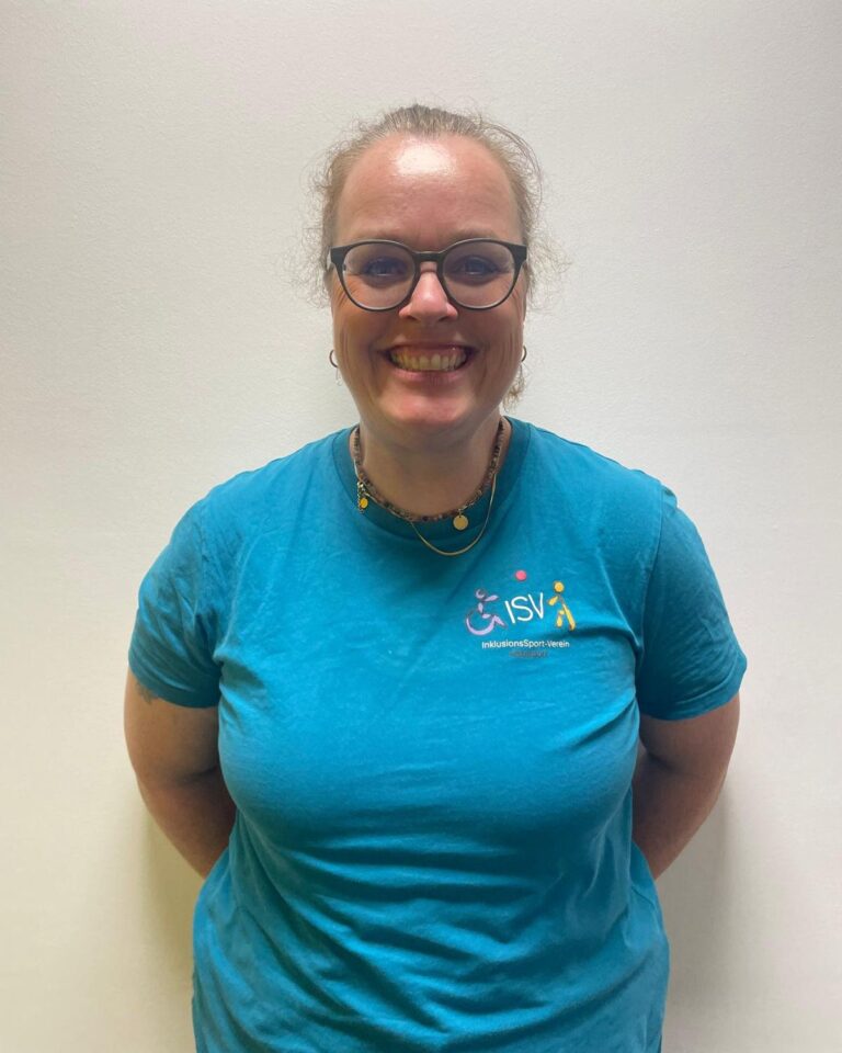 Lächelnde Trainerin des ISV Alsterdorf im Vereins-T-Shirt vor neutralem Hintergrund.