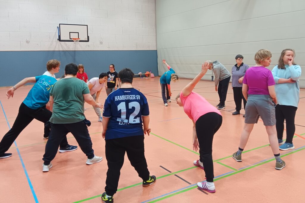 Mehrere Teilnehmende dehnen sich gemeinsam in der Turnhalle und bereiten sich auf das Training vor.