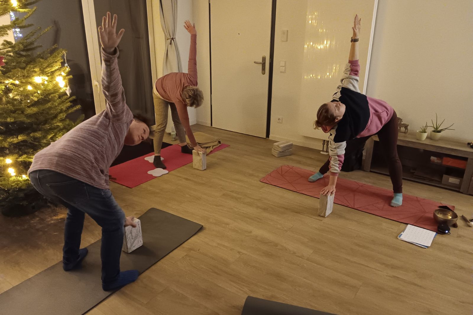 Drei Personen üben eine Yoga-Dehnung auf Matten in einem warm beleuchteten Raum.
