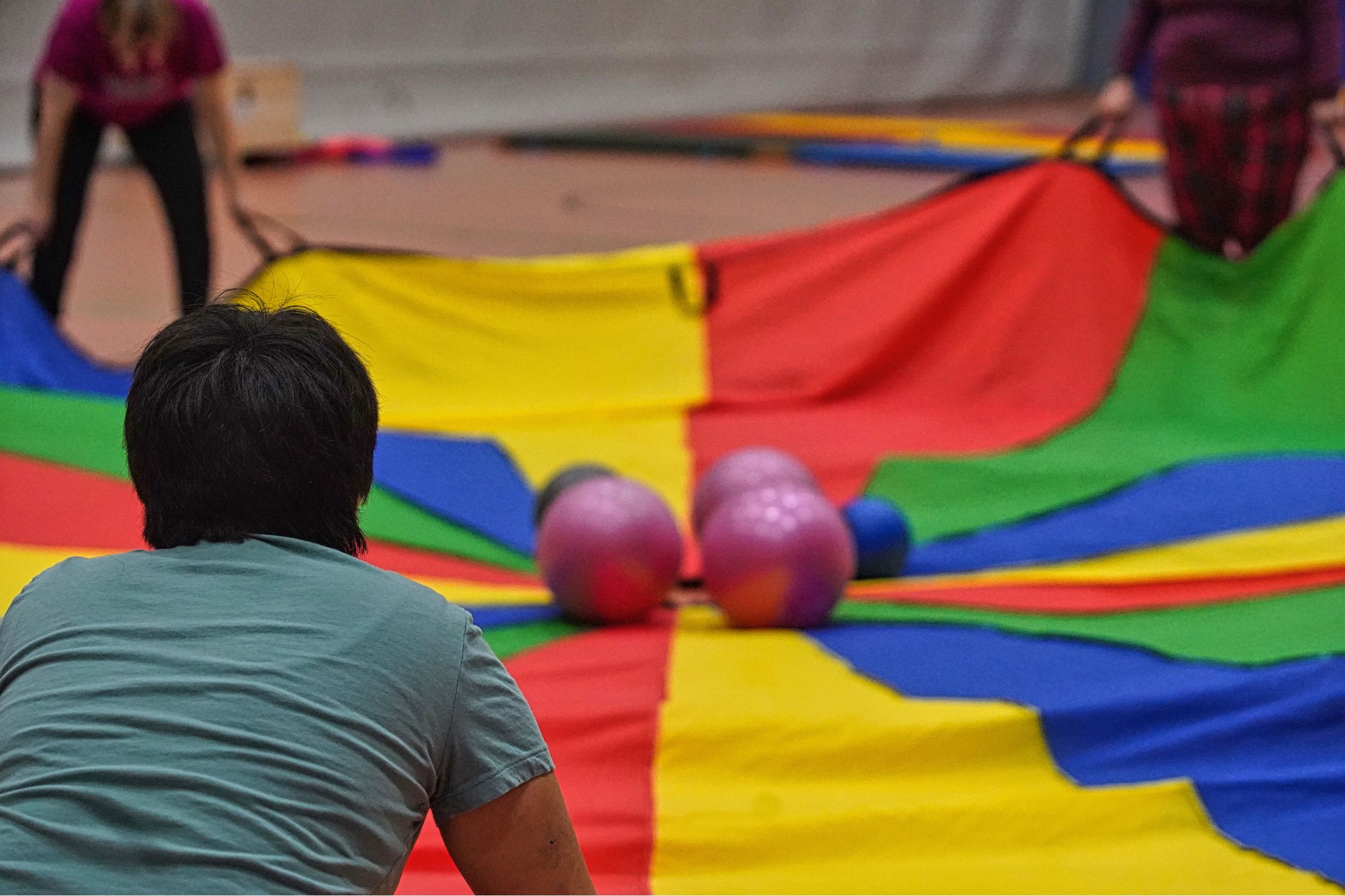 Mehrere Personen bewegen ein großes buntes Schwungtuch, auf dem bunte Bälle hin und her rollen.