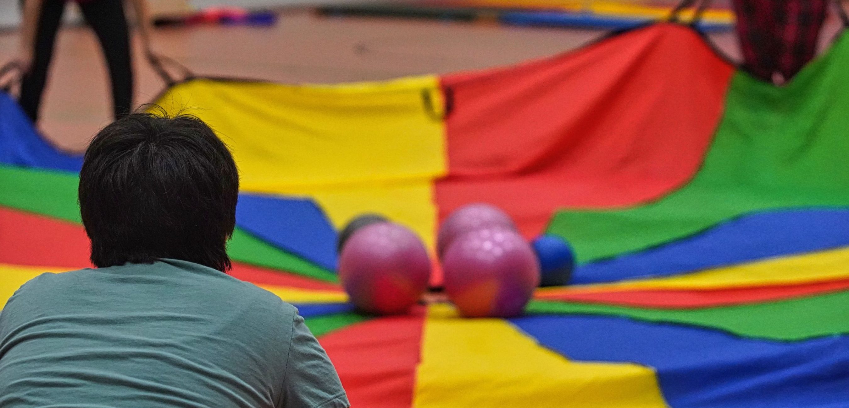 Mehrere Personen bewegen ein großes buntes Schwungtuch, auf dem bunte Bälle hin und her rollen.